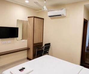 A hotel room with a bed, a TV mounted on the wall, a wardrobe, a chair, and an air conditioning unit. - Deluxe Room Hotel Stay Comfort (Hyderabad)