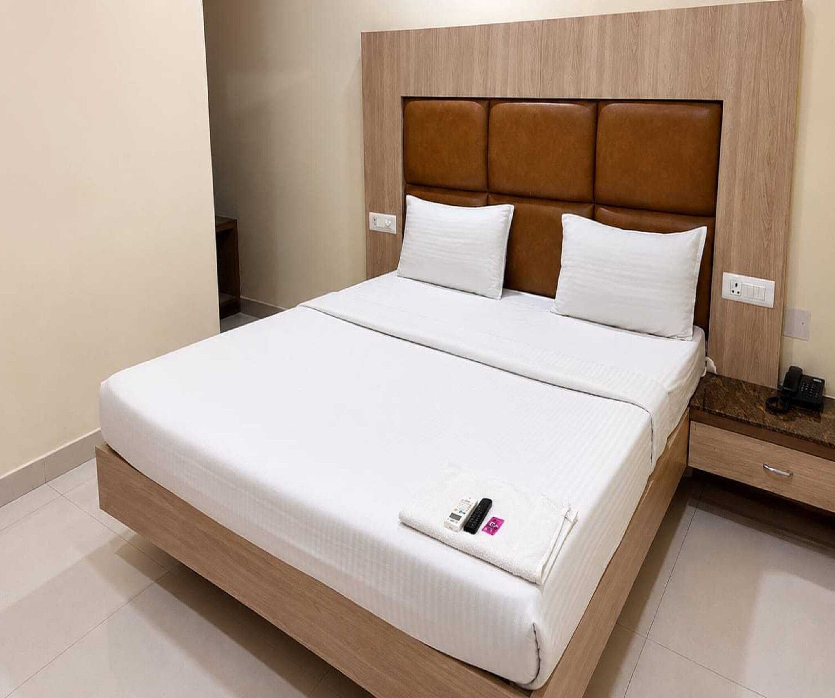 A hotel room with a large bed, a wooden headboard, white bedding, and a bedside table with a phone.