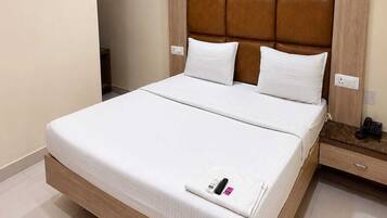 A hotel room with a large bed, a wooden headboard, white bedding, and a bedside table with a phone.