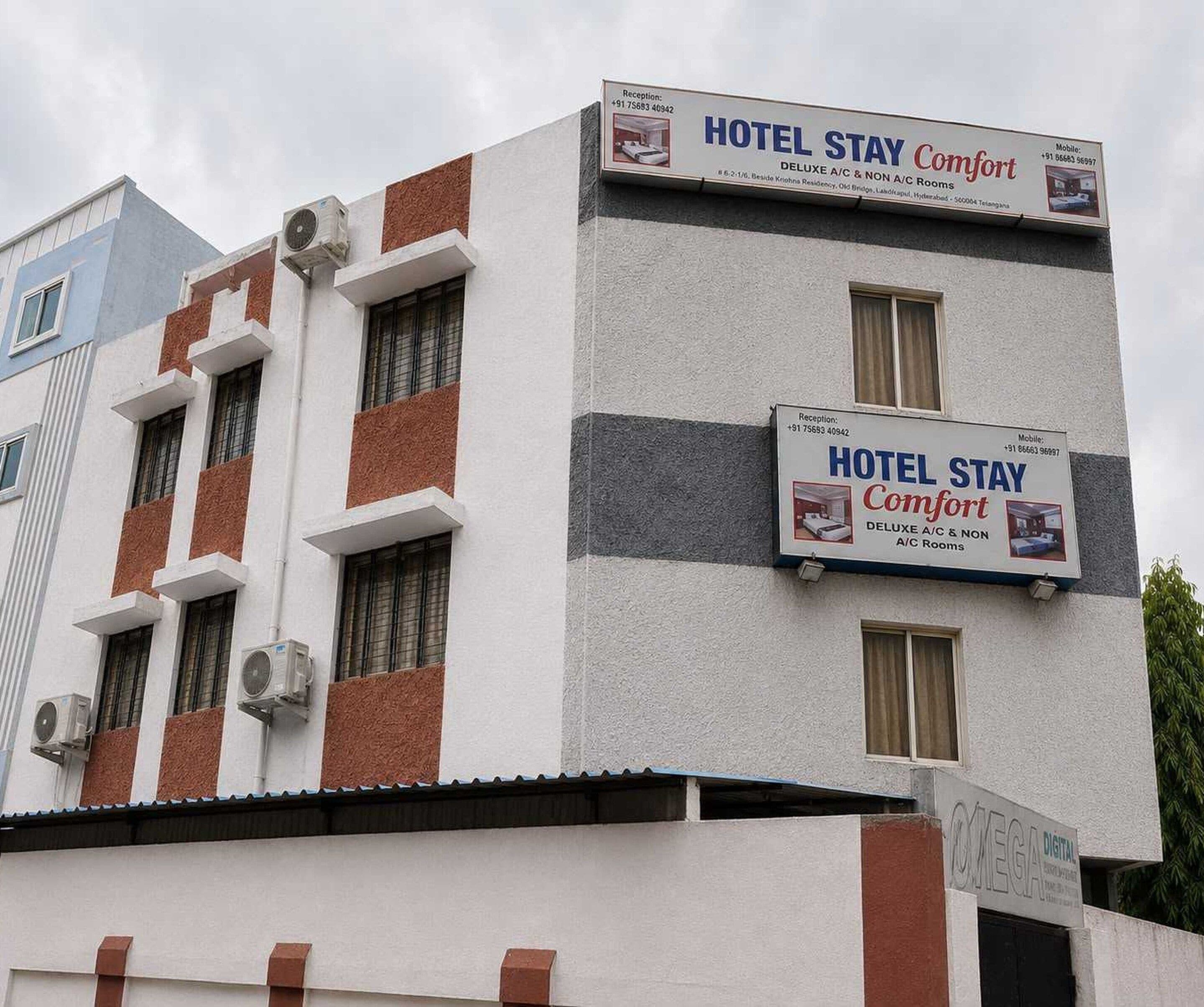 A hotel building with multiple signs advertising 'HOTEL STAY Comfort' and 'DELUXE A/C & NON A/C Rooms'.