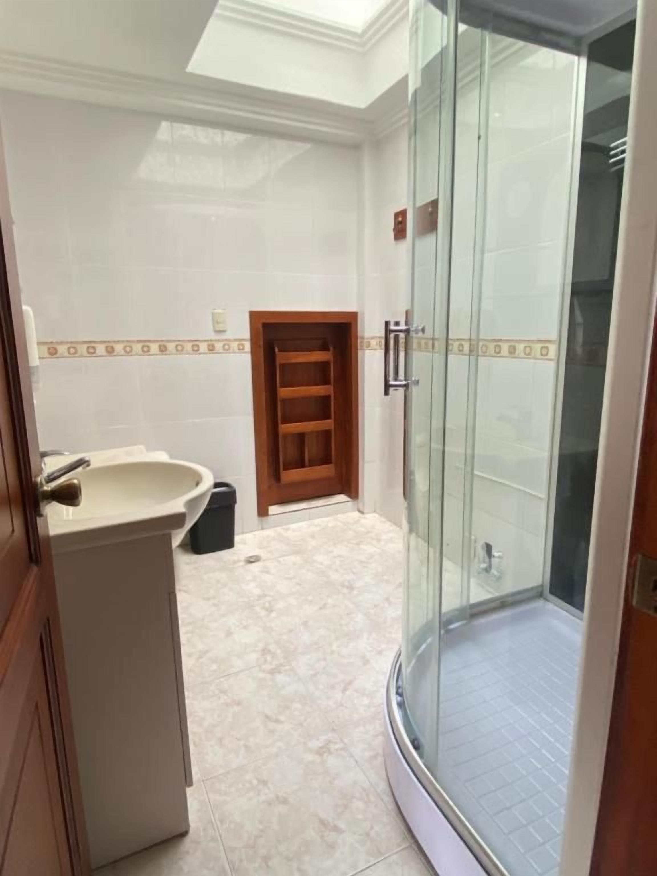 A bathroom with a glass shower enclosure, a sink, and a wooden door.