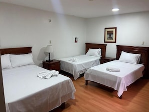 A hotel room with three single beds, each with a wooden headboard, white bedding, and a bedside table with a lamp. - Hotel Coronel (Cuenca)