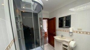 Um banheiro com chuveiro em box de vidro, pia e vaso sanitário.