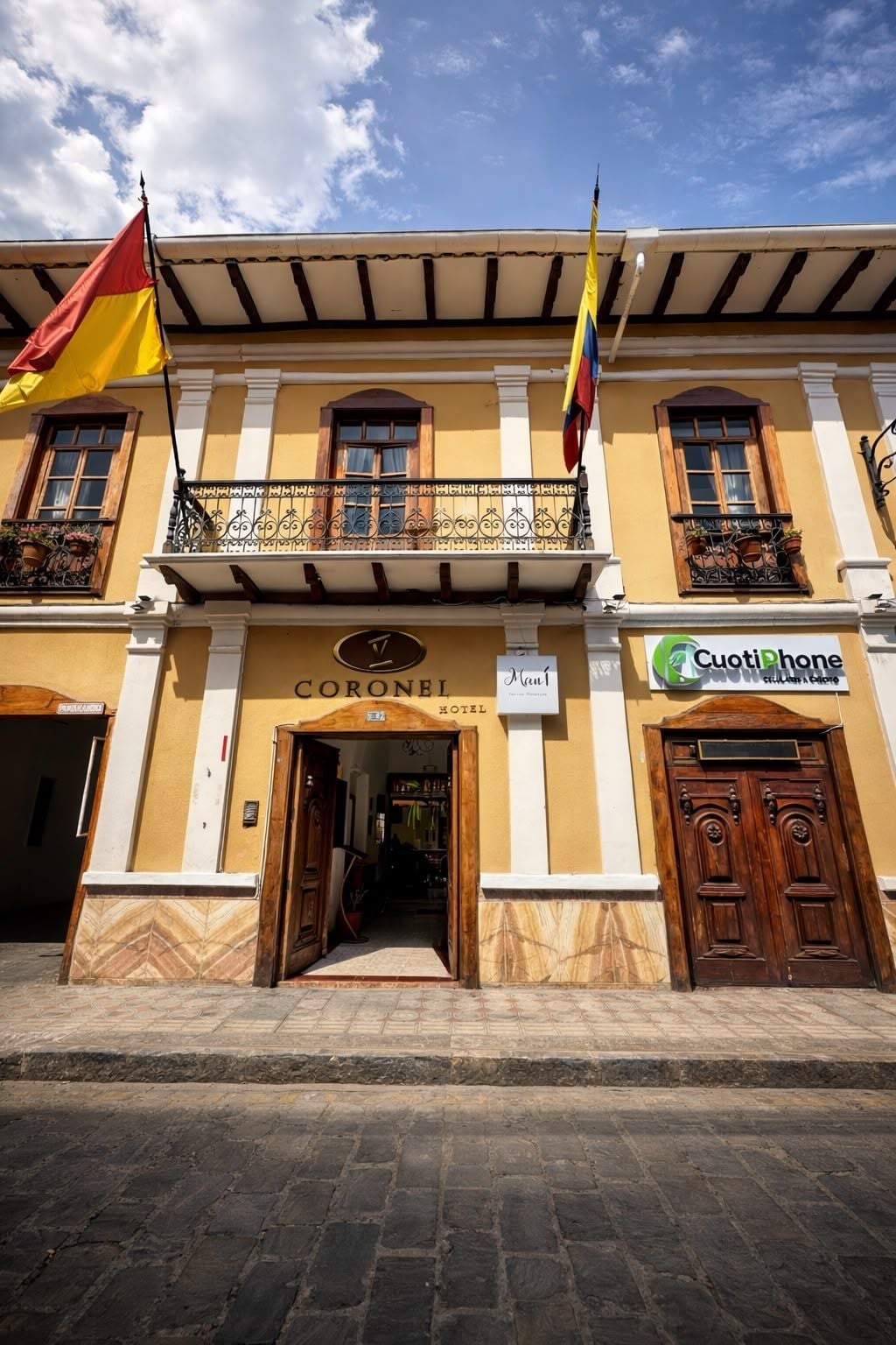 A hotel with a traditional facade, a balcony with wrought iron railings, and a sign for a Cuotiphone store.