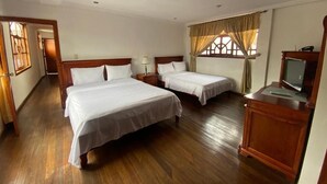Quarto de hotel com duas camas, soalho de madeira, televisão e janela com cortinas.