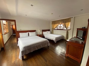 A hotel room with two beds, wooden flooring, a television, and a window with curtains. - Hotel Coronel (Cuenca)