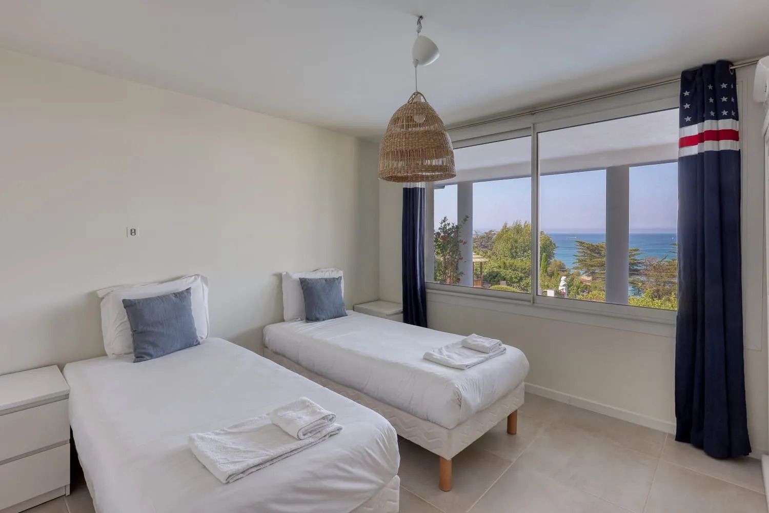 Quarto de hotel com duas camas, uma janela ampla com vista e um lustre.