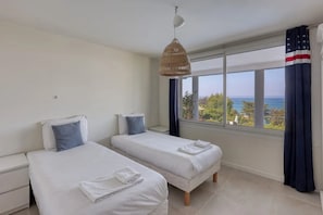 A hotel room with two beds, a large window with a view, and a hanging light fixture.