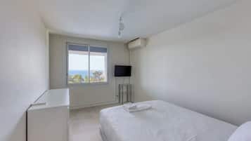 A bedroom with a bed, a desk, a TV, and a window with a view.