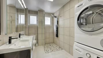 A modern bathroom with a built-in washing machine, a glass shower enclosure, and a large mirror.