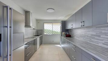 A modern kitchen with stainless steel appliances, grey cabinetry, and a tiled floor.