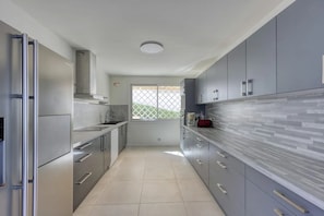 A modern kitchen with stainless steel appliances, grey cabinetry, and a tiled floor.