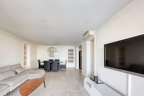 A modern living room with a sofa, coffee table, TV, dining area with chairs, and a large mirror.