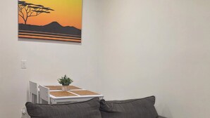 A room with a gray sofa, a painting of a sunset, and a small table with a plant. - Cozy 2BR, 1Bath Suite in NW Calgary, Near Airport. (Calgary)