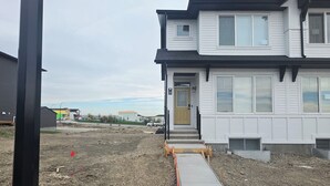 A two-story building with a visible entrance and a concrete pathway leading to the door. - Cozy 2BR, 1Bath Suite in NW Calgary, Near Airport. (Calgary)