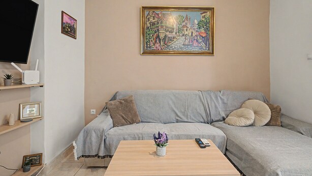 En stue med sofa, sofabord, fjernsyn og et billede på væggen.