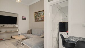 En stue med sofa, sofabord, fjernsyn, et maleri og en vaskemaskine.