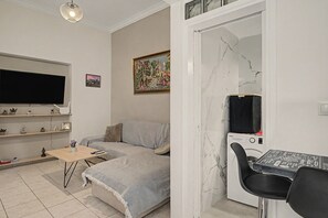 A living room with a sofa, a coffee table, a TV, a painting, and a washing machine. - Apartment 'Colonus' with Shared Terrace, Wi-Fi and Air Conditioning (Αθήνα)