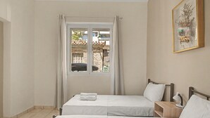 Et hotelværelse med to senge, et vindue med gardiner, et natbord med lampe og et billede i ramme på væggen.