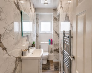 A bathroom with a marble wall, a sink, a toilet, and a shower area. - The Nottingham Hideaway | Stylish Modern Stay (Nottingham)