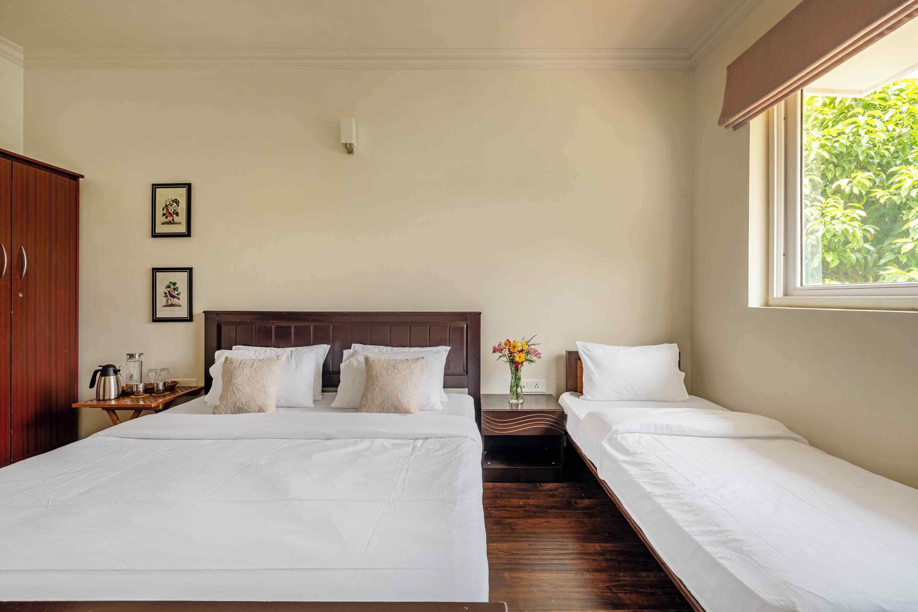 Quarto de hotel com duas camas de solteiro, um guarda-roupa de madeira, uma mesa de cabeceira com cafeteira e janela com vista para o verde.