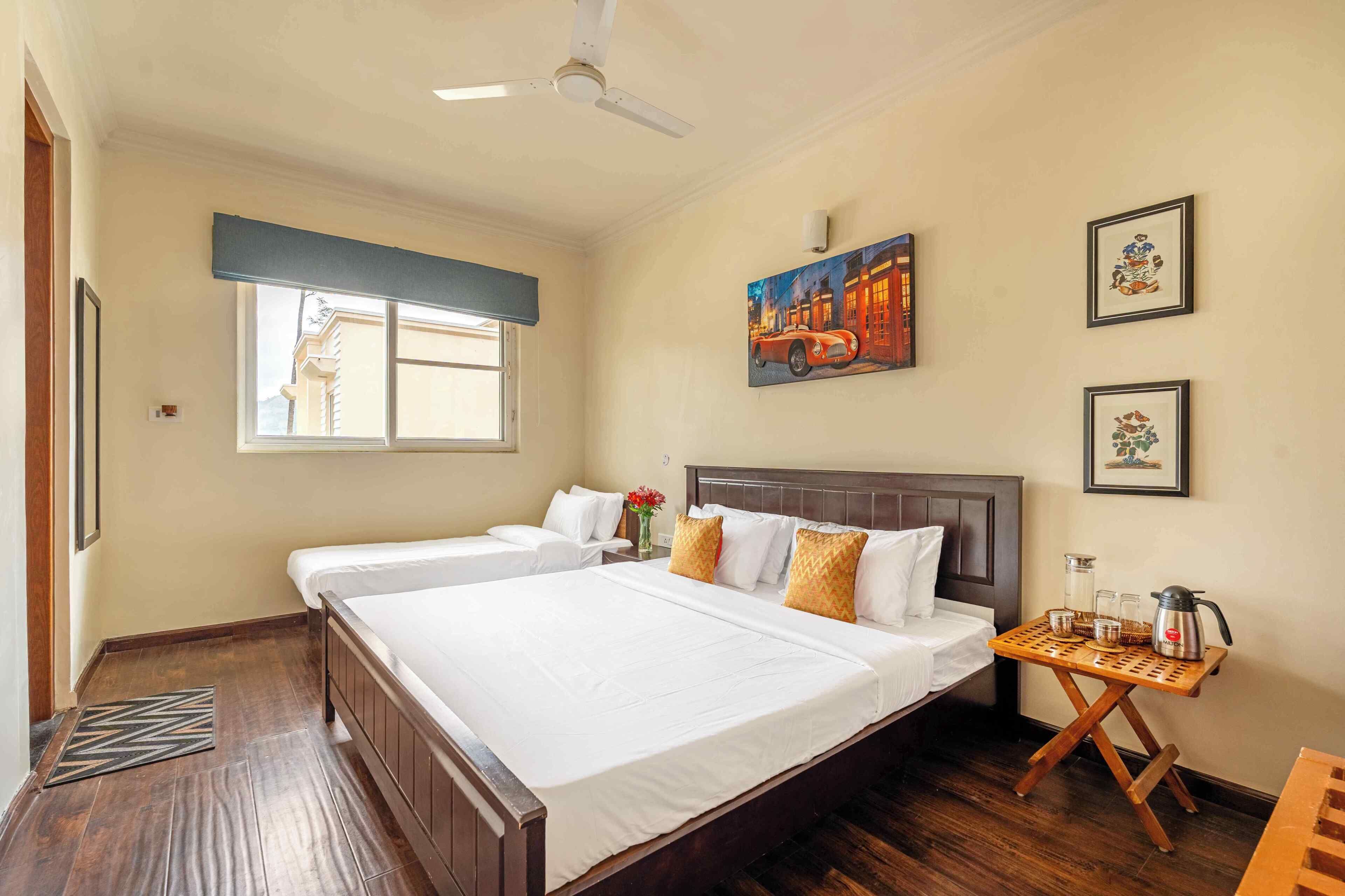 Habitación de hotel con dos camas, un ventilador de techo, una ventana con vistas y una mesita con cafetera.