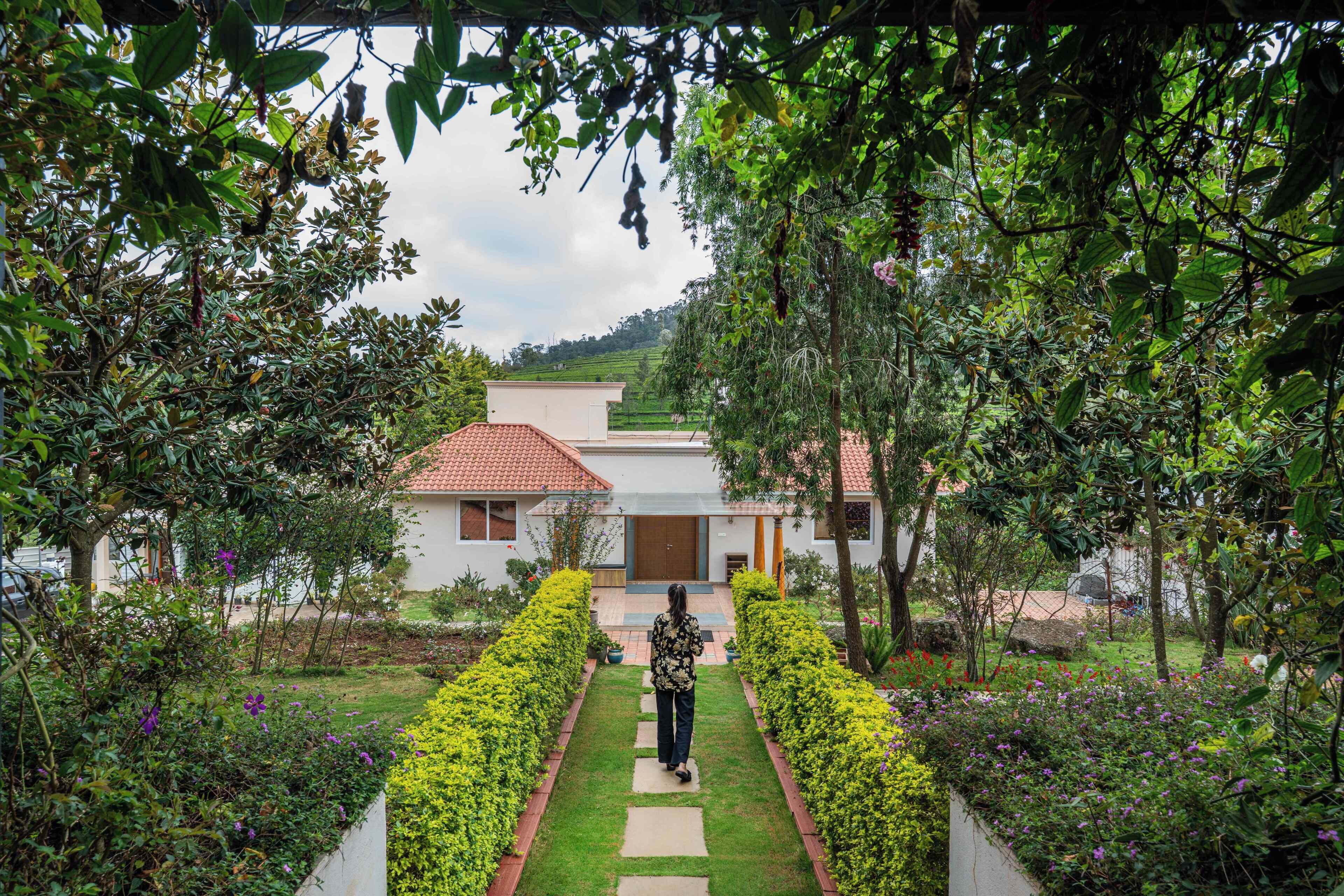 Un sendero conduce a una casa de techo de tejas, rodeada de abundante vegetación y un jardín cuidado.