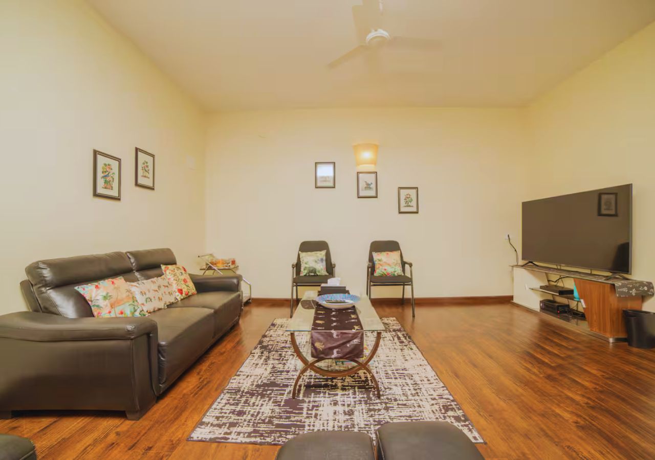 Una sala de estar con sofá, dos sillones, una mesa de centro, televisor y cuadros en la pared.