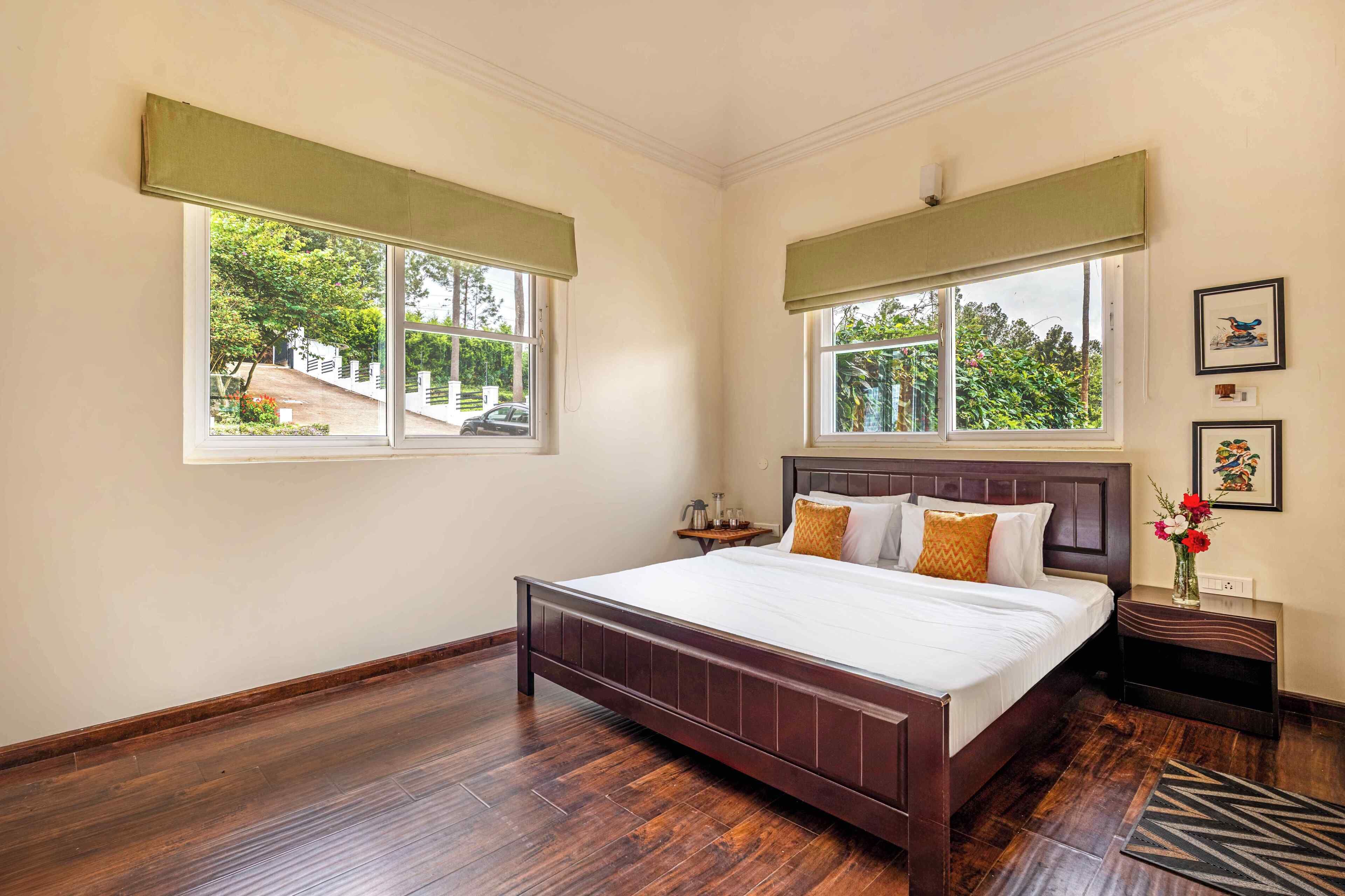 Un dormitorio con una cama de madera, dos ventanas con cortinas verdes, una mesita de noche y un aplique de pared.