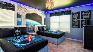 A bedroom with two beds, Star Wars-themed bedding, a space-themed wall mural, and Star Wars posters.