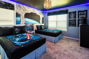 Ein Schlafzimmer mit zwei Betten, Star Wars-Bettwäsche, einer Wandmalerei zum Thema Weltraum und Star Wars-Postern.
