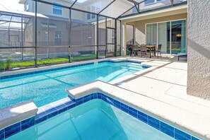 A swimming pool with a glass enclosure, a patio area with outdoor furniture, and a view of the surrounding buildings. - High Ceiling/Themed BR/SPA 22089 (Kissimmee)