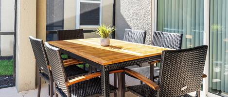 A wooden table with six chairs, a potted plant, and a window with blinds.