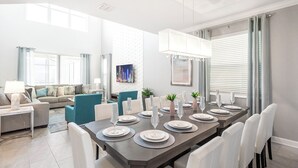 A modern dining area with a long table set for six, surrounded by white chairs.