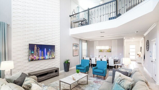 A spacious living room with a large flat-screen TV, a dining area, and a staircase leading to an upper level.