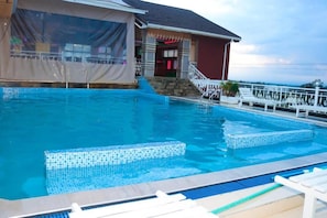 Una piscina con borde de azulejos, zona techada con escalones y barandilla blanca.