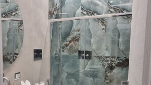Ett modernt badrum med en duschkabin i marmor, en stor spegel och ett handfat med förvaringsutrymme.