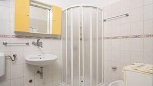 Un baño con un lavamanos blanco, un espejo encima, un mueble amarillo, una cabina de ducha y un inodoro.