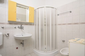 A bathroom with a white sink, a mirror above it, a yellow cabinet, a shower enclosure, and a toilet. - A1 - Cozy apartment with pool and spacious terrace, 2 min walk to beach (Omiš)
