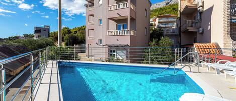 A swimming pool with a metal railing, surrounded by buildings with balconies.