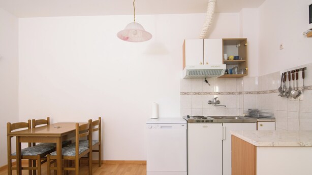 Una cocina funcional con lavavajillas, pileta y una mesa de madera con sillas.