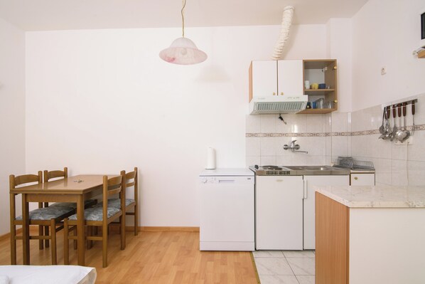 A compact kitchen with a dishwasher, a sink, and a wooden dining table with chairs. - A1 - Cozy apartment with pool and spacious terrace, 2 min walk to beach (Omiš)