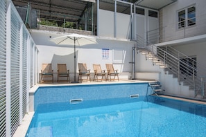 A swimming pool with a tiled edge, wooden lounge chairs, a covered area with a metal roof, and a staircase leading to an upper level. - A1 - Cozy apartment with pool and spacious terrace, 2 min walk to beach (Omiš)