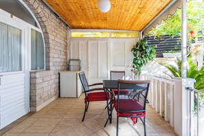 A covered patio area with a brick wall, a white door, and a small white refrigerator. There are two chairs with red cushions and a table. - A1 - Cozy apartment with pool and spacious terrace, 2 min walk to beach (Omiš)