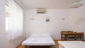 Un dormitorio con cama, una mesa de comedor, sillas, aire acondicionado y un cuadro en la pared.