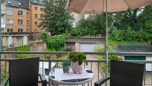 A balcony with wicker chairs, a table with a placemat, a potted plant, and a brown umbrella.