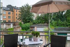 A balcony with wicker chairs, a table with a placemat, a potted plant, and a brown umbrella.