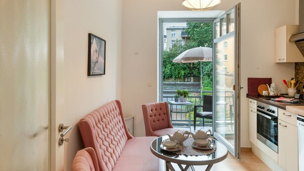 A compact kitchen with modern appliances, a dining area with a table set for tea, and a view of a balcony with greenery.