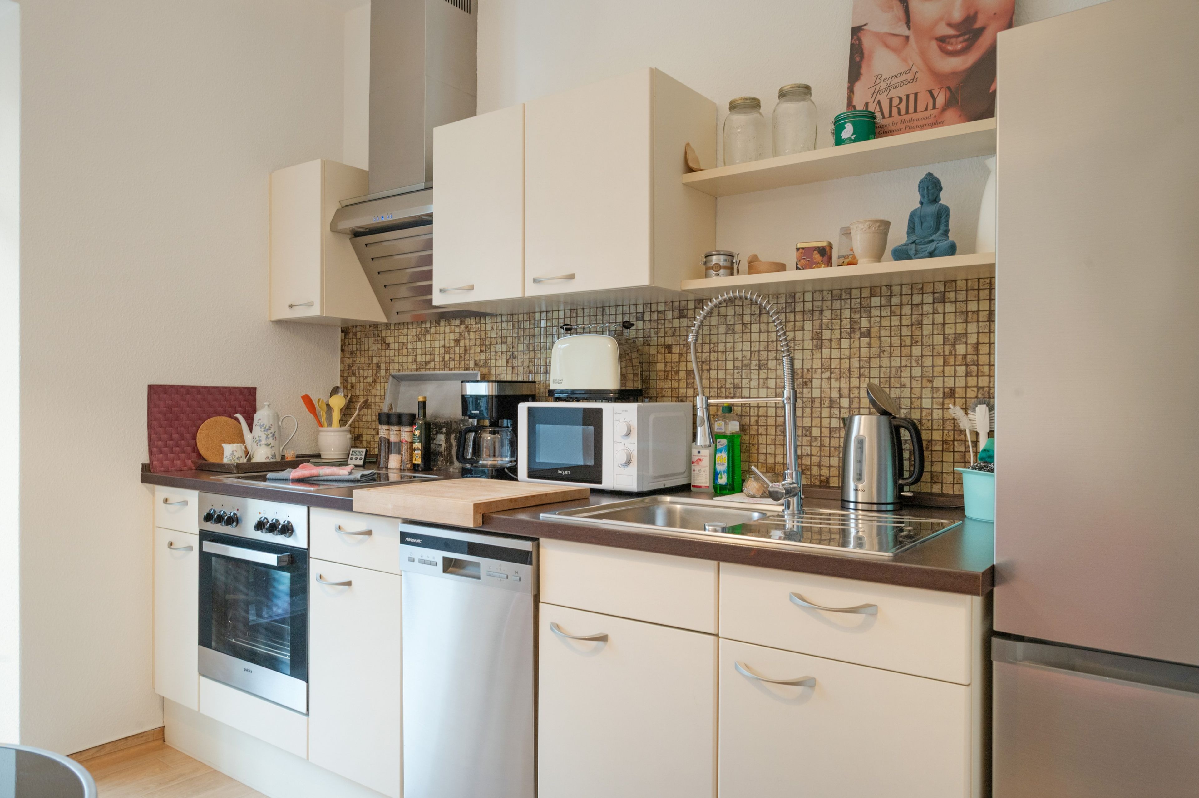 A modern kitchen with white cabinetry, a built-in oven, a dishwasher, a microwave, and a coffee maker.