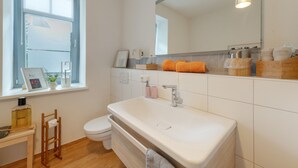 A modern bathroom with a large white sink, a toilet, and a window with blinds.